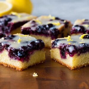 Glazed lemon blueberry bars cut into squares with white drizzle and fresh blueberries on parchment