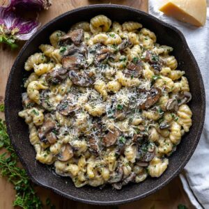 Creamy roasted garlic and mushroom pasta in a black skillet with fresh thyme, parmesan, and cracked pepper
