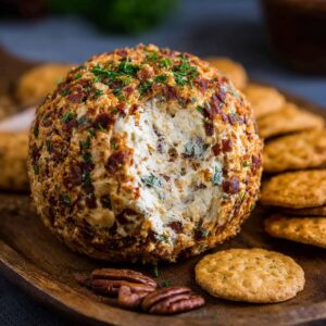 Cowboy cream cheese ball coated in crispy bacon, shredded cheddar, and chopped scallions on a wooden board with crackers