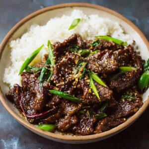 Mongolian beef with crispy edges, glossy sweet-soy sauce, sliced scallions, and steamed white rice on a black plate
