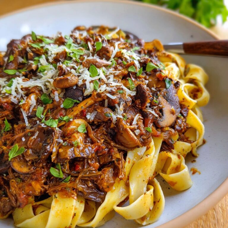 Mushroom ragu over wide pappardelle pasta with deep red wine sauce, fresh thyme, parmesan shavings, and cracked pepper
