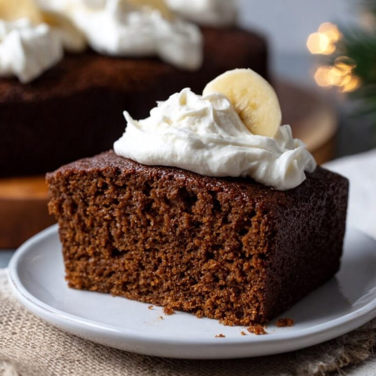 Gingerbread cake with white powdered sugar dusting, candied orange peel, fresh rosemary, and visible spice flecks in dark brown crumb