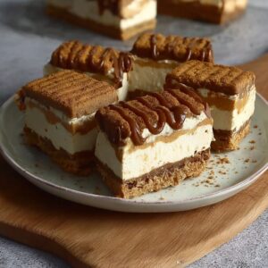 Ice cream sandwich cake on a serving plate with stacked ice cream sandwiches, layers of cool whip, chocolate sauce drizzle, sprinkles, cherries