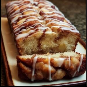 Cinnamon roll bread with icing on a wooden board, sliced loaf revealing soft cinnamon-sugar swirl, generous white vanilla icing drizzled across the top