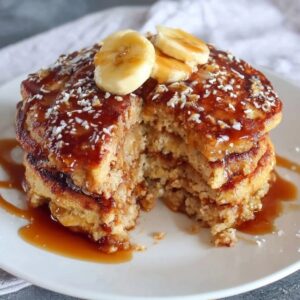 Stack of fluffy oatmeal pancakes on a wooden plate, golden brown edges, pat of butter melting on top, drizzle of maple syrup running down the sides, fresh blueberries scattered around, bright morning light