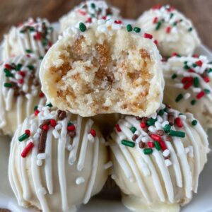 Sugar cookie truffles arranged on a white plate, white chocolate coated balls with red and green sprinkles, festive holiday styling, snowflake doily underneath